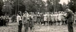 Czarno-biała fotografia grupowa harcerzy z Konstantynowa Łódzkiego sprzed 1975 roku. Grupa stoi w równych rzędach w mundurach harcerskich. W tle las.