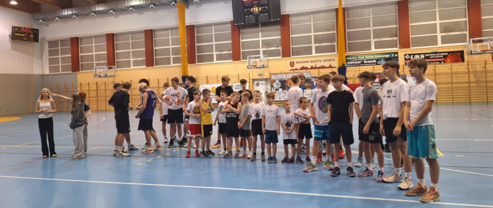 Uczestnicy rozgrywek stojący na środku hali sportowej