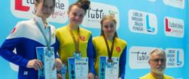 Zdjęcie przedstawia trzy uśmiechnięte zawodniczki stojące na podium: druga od lewej stoi Anna Wilk, a trzecia Milena Sosnówka. Po prawej stronie stoi trener Fali Grzegorz Mazurek. Zawodniczki maja na szyjach zawieszone medale, a w rękach trzymają dyplomy.
