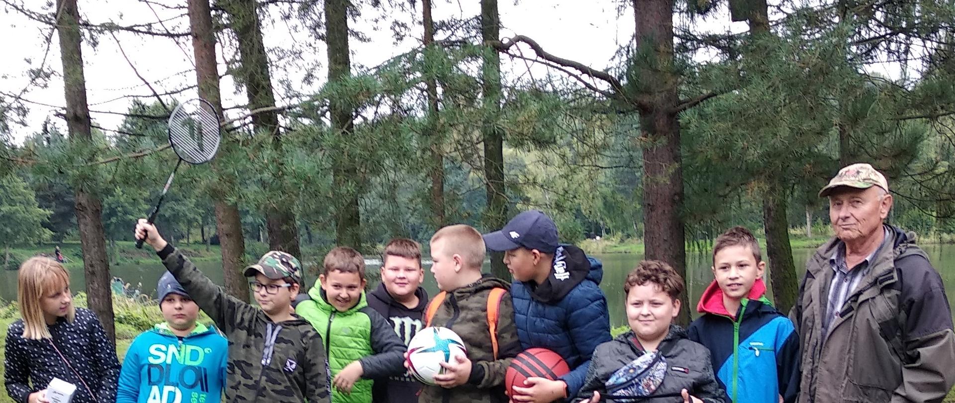 Nagrodzeni finaliści zawodów z prezesem Koła Janem Cieślarem. Na zdjęciu grupa dzieci z nagrodami. Jeden chłopak prezentuje rakietę do badmintona