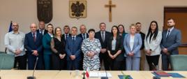 Zdjęcie przedstawia nowego Wójta pana Tomasza Rajce oraz nowo wybranych radnych pozujących do zdjęcia na sali obrad w urzędzie gminy podczas I sesja Rady Gminy 