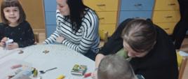 Uczestnicy warsztatów siedzą przy stole, dekorują pierniczki