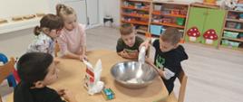 Wspólne pieczenie pierniczków - dzieci siedzą przy stole i wykonują czynności związane z przygotowaniem ciasteczek. Pozują przy tym do zdjęć