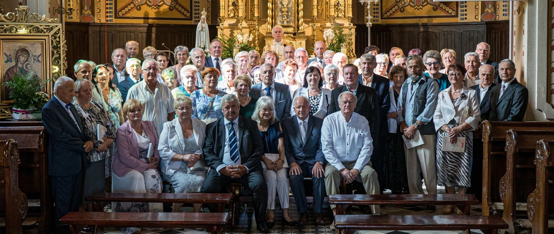 Fotografia grupowa wykonana w kościele przed ołtarzem, przedstawiająca uczestników uroczystości jubileusz 50-lecia pożycia małżeńskiego