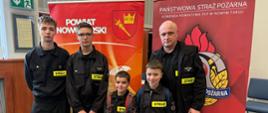 Czwórka reprezentantów z Rokicin Podhalańskich wraz z opiekunem. Stoją przed roll upami Powiatu Nowotarskiego oraz Państwowej Straży Pożarnej 