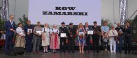 Zamarscy społecznicy z otrzymanymi podziękowaniami. Grupa osób stoi na scenie. 