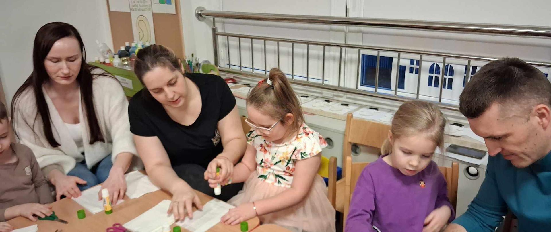 Rodzice z dziećmi siedzą przy stole, przygotowują gwiazdy z papieru