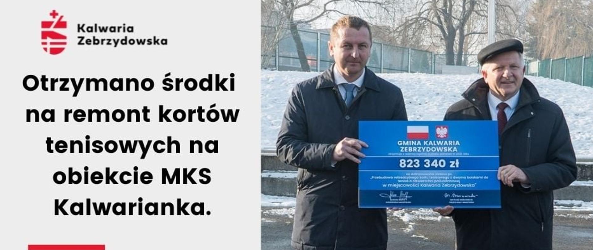 Burmistrz Augustyn Ormanty i radny Marcin Zadora stoją na płycie kortu tenisowego w Kalwarii trzymają symboliczny czek informujący o kwocie dofinansowania