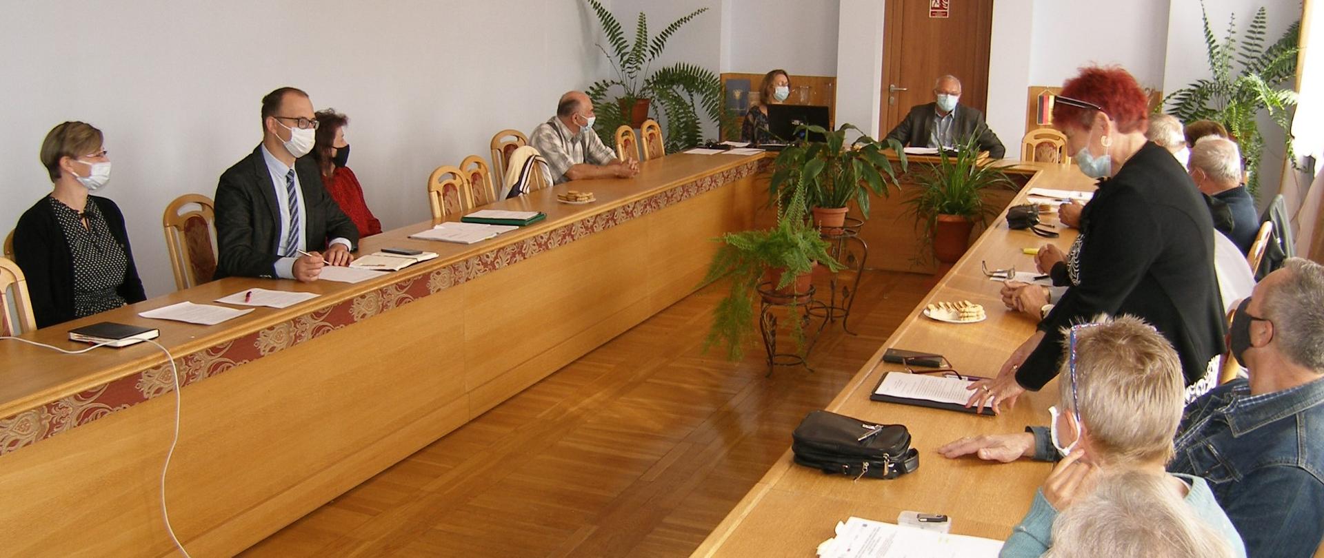 Obrady w sali sesyjnej Urzędu Gminy Hażlach. Osoby zajmują miejsca siedzące. Jedna osoba mówi na stojąco 