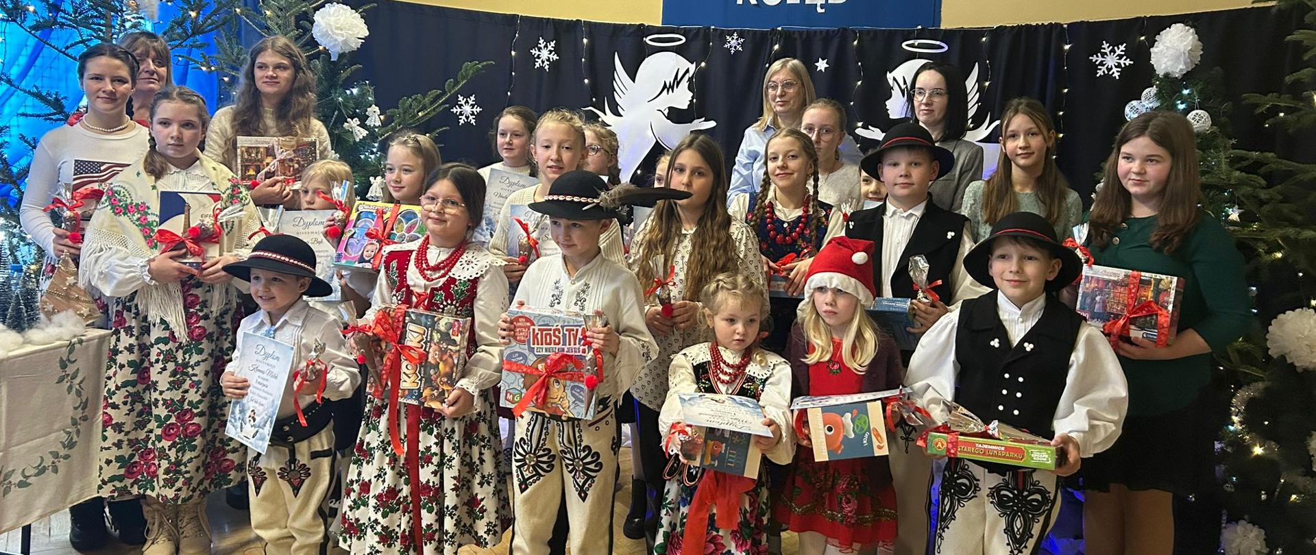 Grupa laureatów wraz z opiekunami na scenie po odbiorze upominków. Dzieci ubrane w góralskie stroje.