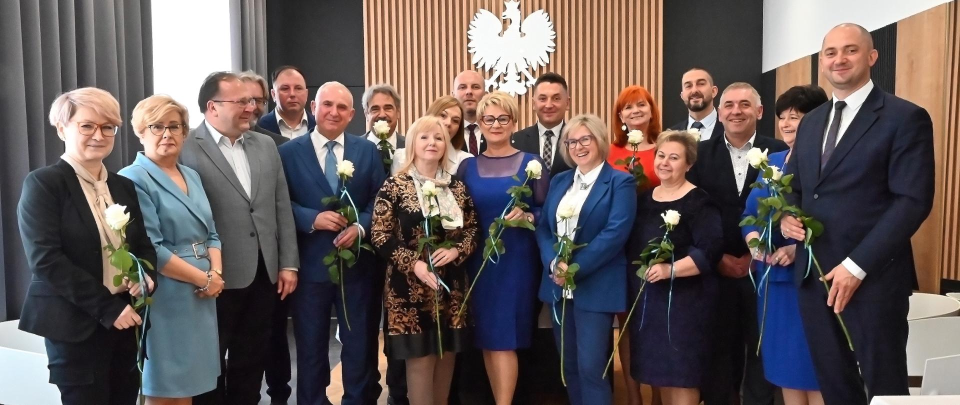 Zdjęcie grupowe radnych rady miejskiej, włodarzy oraz współpracowników. W tle godło Polski.