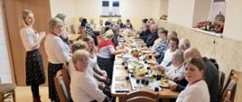 Panie z koła gospodyń wiejskich oraz zaproszeni goście siedzą przy stole i jedzą poczęstunek. 