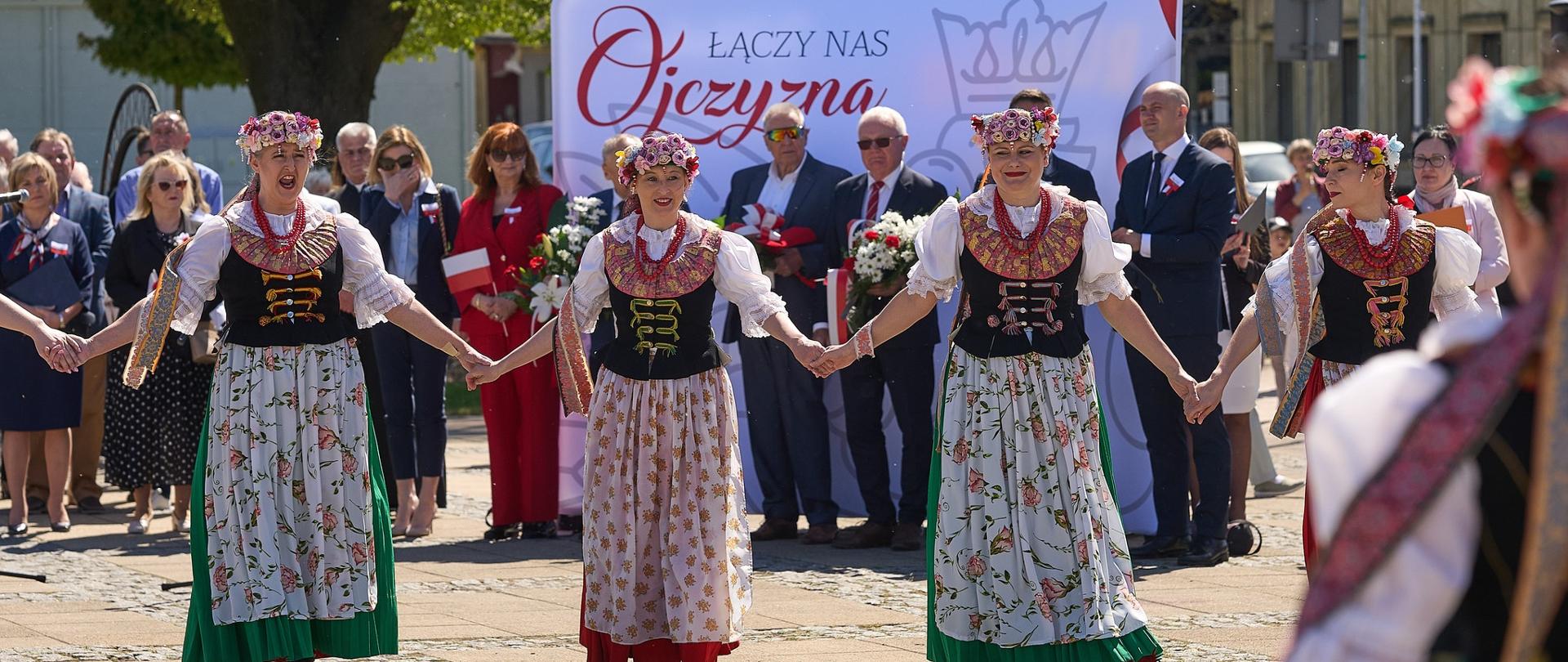 Tancerze w strojach ludowych trzymają się za ręce. 