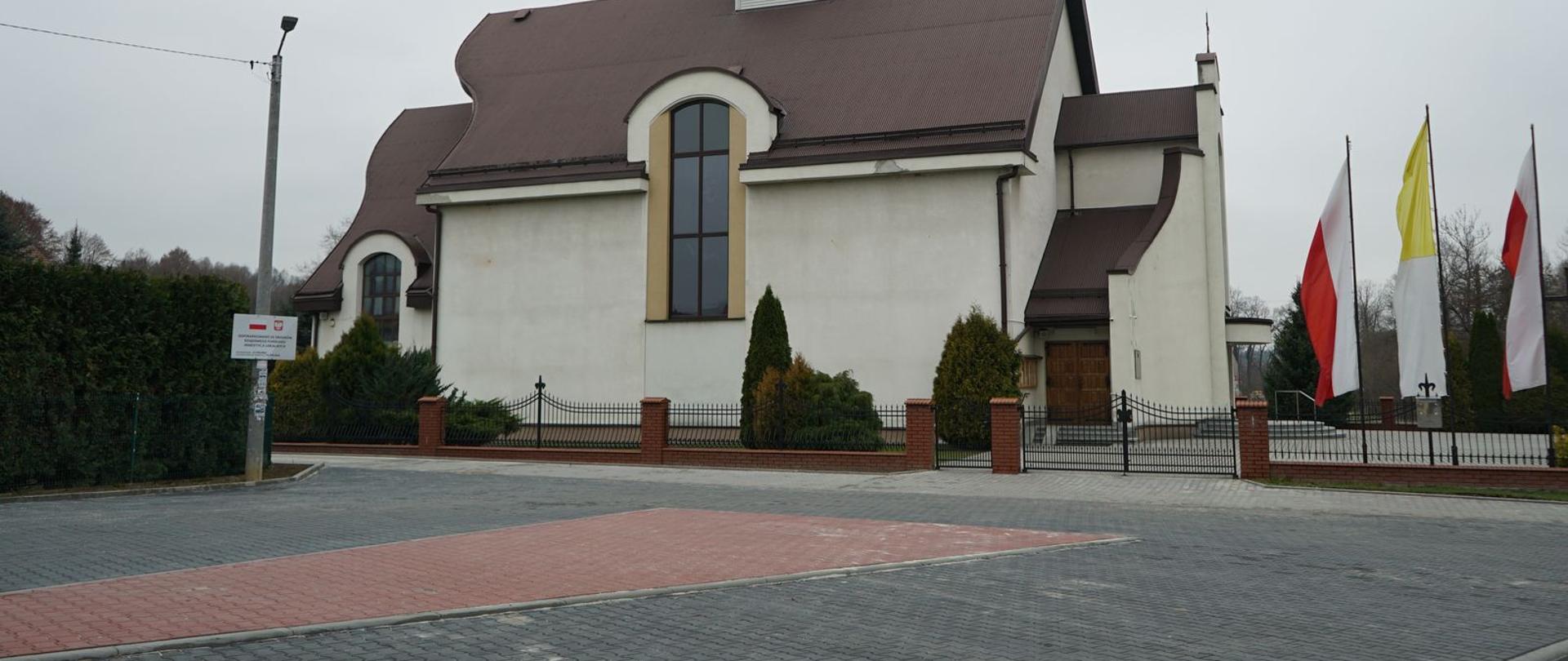 Zdjęcie parkingu, w tle kościół parafialny. 