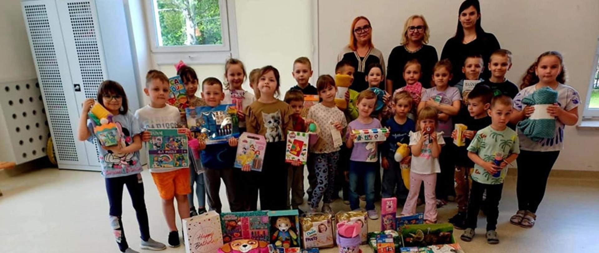 Dzieci wraz z dyrekcją przedszkola pozują do zdjęcia, prezentując zebrane dary
