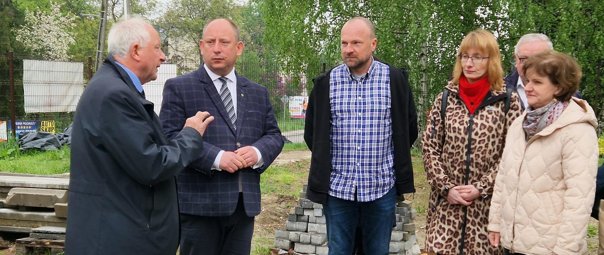 Na zdjęciu widzimy Burmistrza Miasta Kalwarii Zebrzydowskiej Augustyna Ormantego, Wojewodę Małopolskiego Krzysztofa Jana Klęczara, Dyrektor Zespołu Szkół nr 1 w Kalwarii Zebrzydowskiej Marię Mlak oraz reprezentantów wykonawcy remontu szkoły w tle widać drzewa z zielonymi liśćmi oraz elementy kostki brukowej i innych materiałów budowlanych