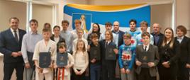 Grupa sportowców z dyplomami wraz z Panem Wójtem Gminy Raba Wyżna, Panią Skarbik, Panem Przewodniczącym Rady Gminy i członkowie Komisji Oświaty, Kultury, Sportu i Ochrony Socjalnej Rady Gminy Raba Wyżna stoją na tle ścianki Gminy Raba Wyżna 