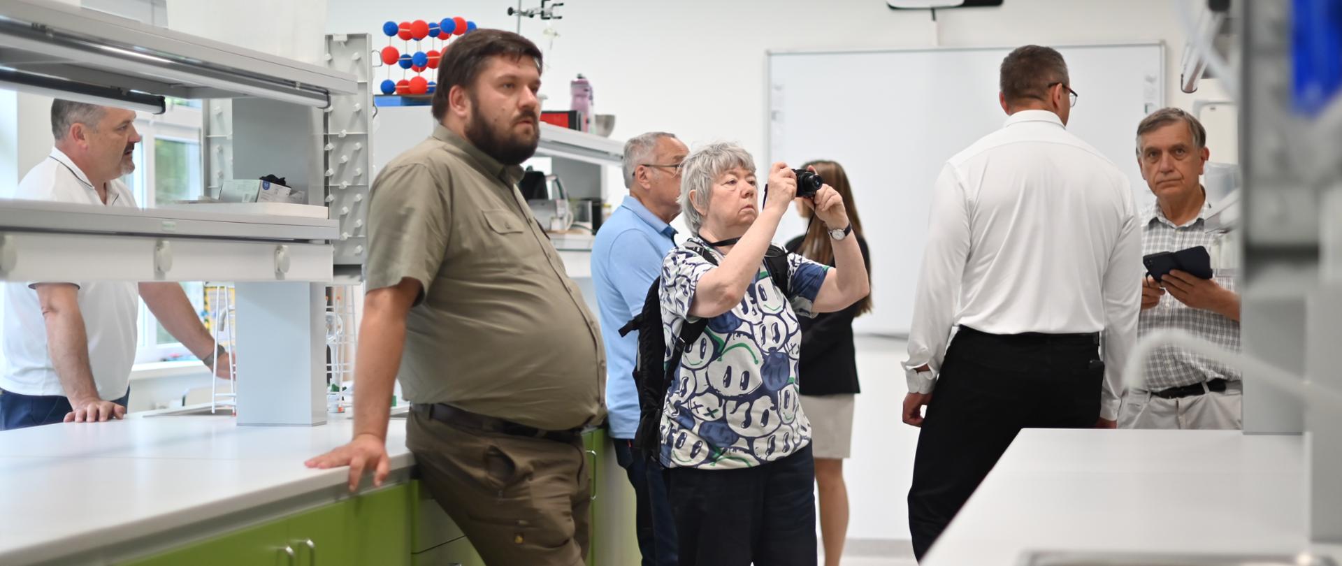 Kilka osób w pracowni chemicznej w szkole, oglądają pomieszczenie i robią zdjęcia.