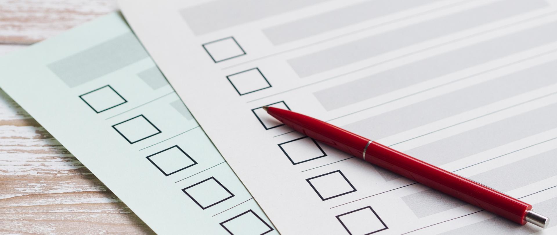 Zdjęcie długopisu leżącego na dwóch kartach z kratkami do zaznaczenia