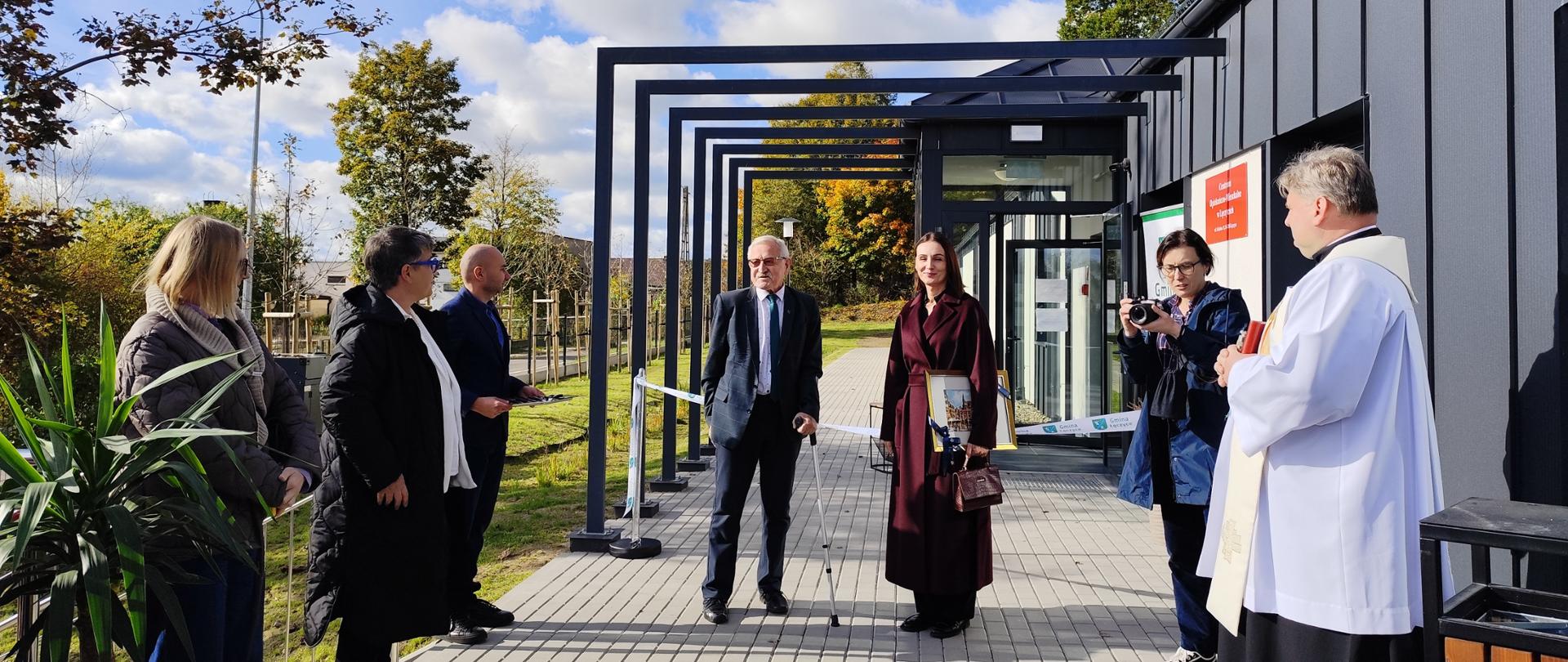 Grupa osób stojących przed wejściem do budynku, które jest zablokowane wstęgą