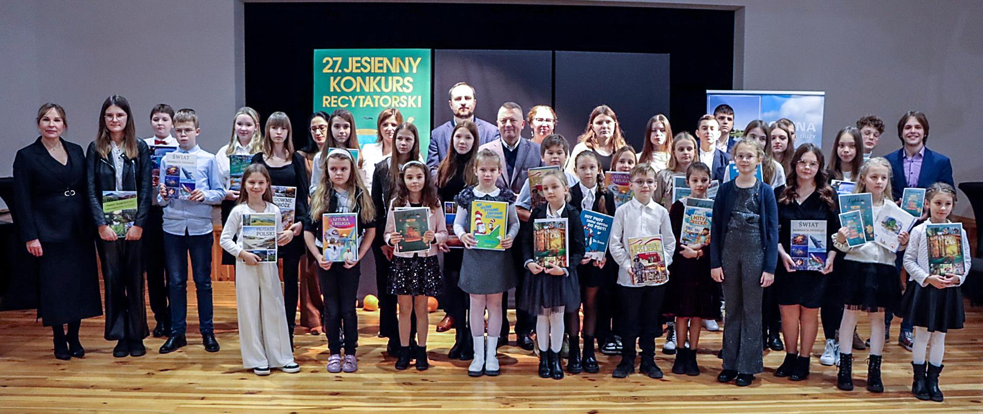 Zdjęcie grupowe uczestników i organizatorów konkursu. Młodzież biorąca udział w konkursie trzyma w dłoniach dyplomy i nagrody.