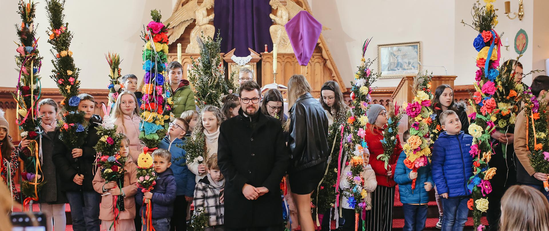 Zdjęcie przedstawia uczestników konkursu z palmami pozujących do zdjęć na tle ołtarza w kościele parafialnym w Bielance
