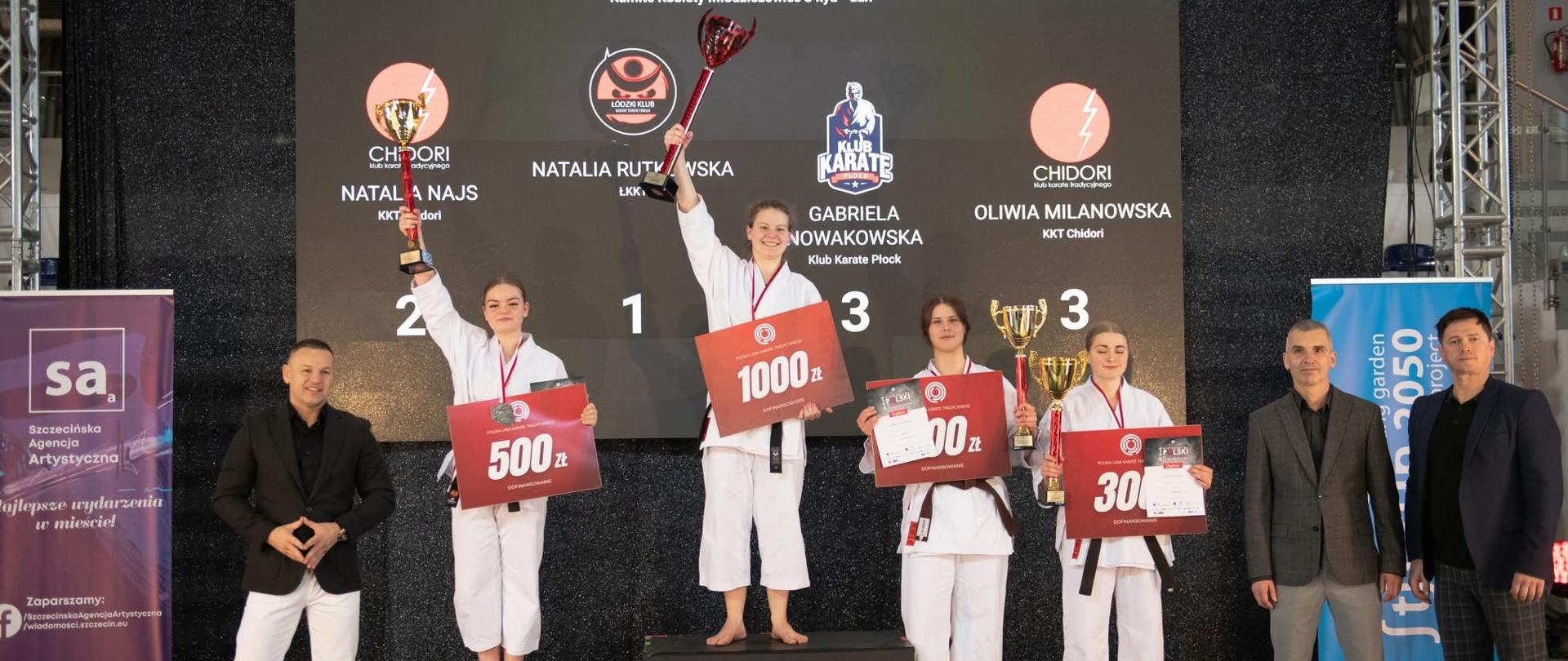 Cztery zawodniczki w kategorii młodzieżowiec stoją na wywalczonych przez siebie stopniach podium. Dziewczęta trzymają w rękach bony upominkowe, dyplomy oraz puchary. Na drugim stopniu podium stoi Natalia Najs. Z tyłu, za zawodniczkami, znajduje się duża czarna tablica, na której zostały wyświetlone imiona, nazwiska oraz nazwy klubów zdobywczyń medali. Po lewej stronie podium stoi mężczyzna ubrany w czarną marynarkę i białe spodnie, zaś po prawej stronie podium stoi dwóch mężczyzn w ciemnych marynarkach i spodniach.