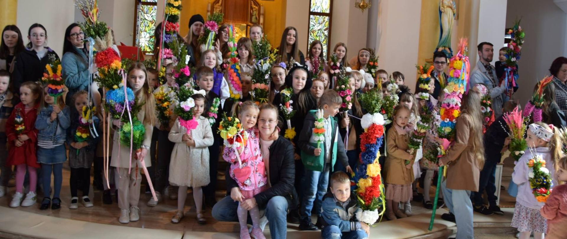 Uczestnicy konkursu z palmami w dłoniach pozują przed obrazem Jana Pawła II 
