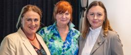 Trzy kobiety stoją obok siebie i pozują do zdjęcia podczas spotkania w sali widowiskowej.