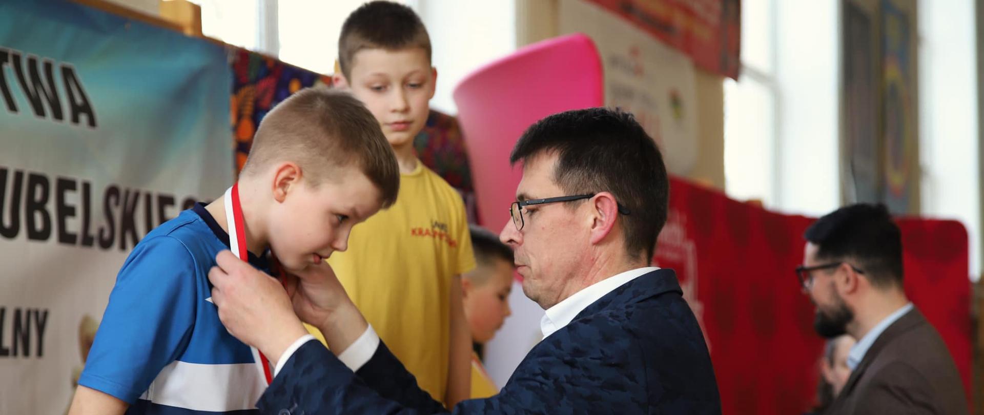 Przewodniczący Rady Powiatu w Kraśniku Jacek Dubiel podczas zakładania medalu na szyję jednemu z zawodników stojących na podium