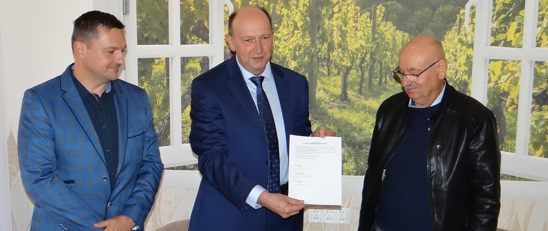 Sygnatariusze aktu założycielskiego Stowarzyszenia „Cieszyński Szlak Wina”. Trzy osoby pozują z podpisanym dokumentem.