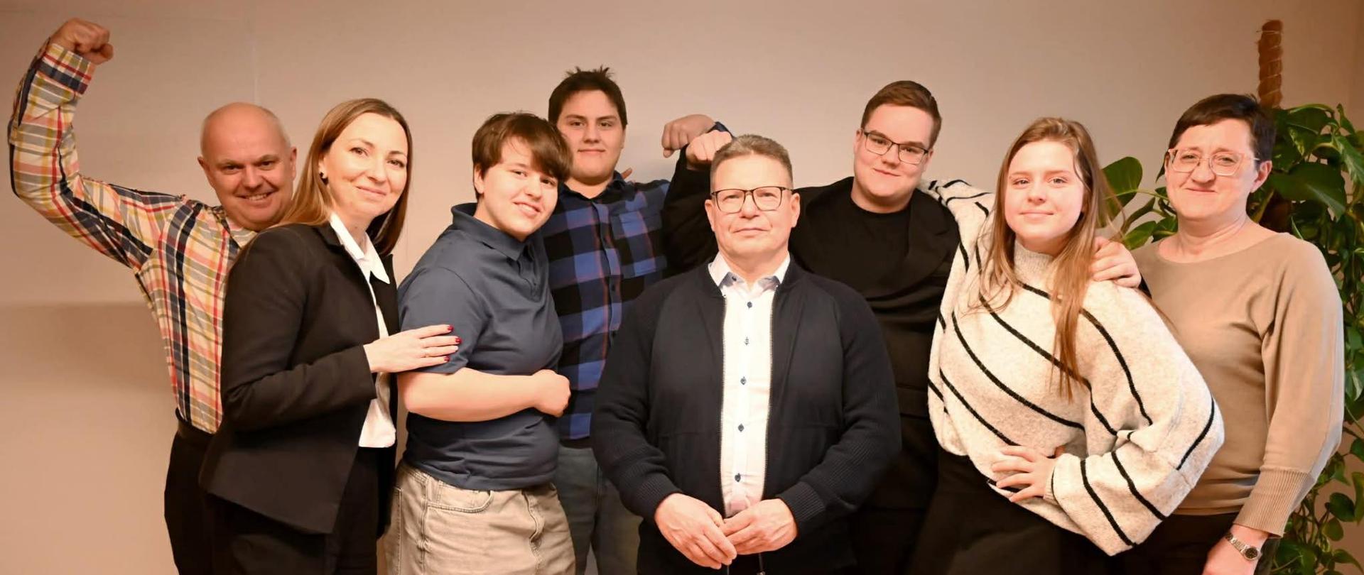 Grupowe zdjęcie zespołu – dziewięć osób stojących razem w pomieszczeniu, uśmiechniętych, w swobodnych pozach.