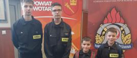 Czwórka reprezentantów z Rokicin Podhalańskich. Stoją przed roll upami Powiatu Nowotarskiego oraz Państwowej Straży Pożarnej 