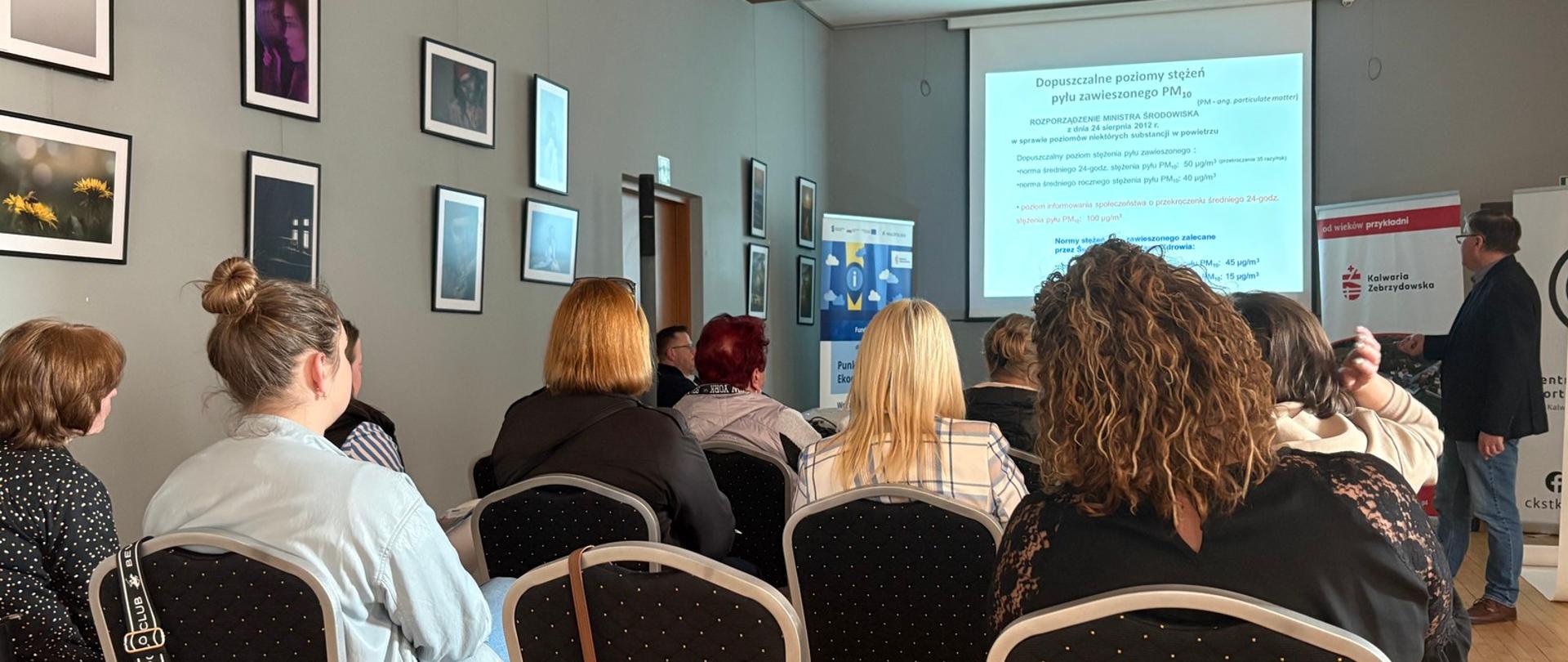 Siedzący na krzesłach uczestnicy spotkania oglądają prezentację wyświetlaną na ekranie