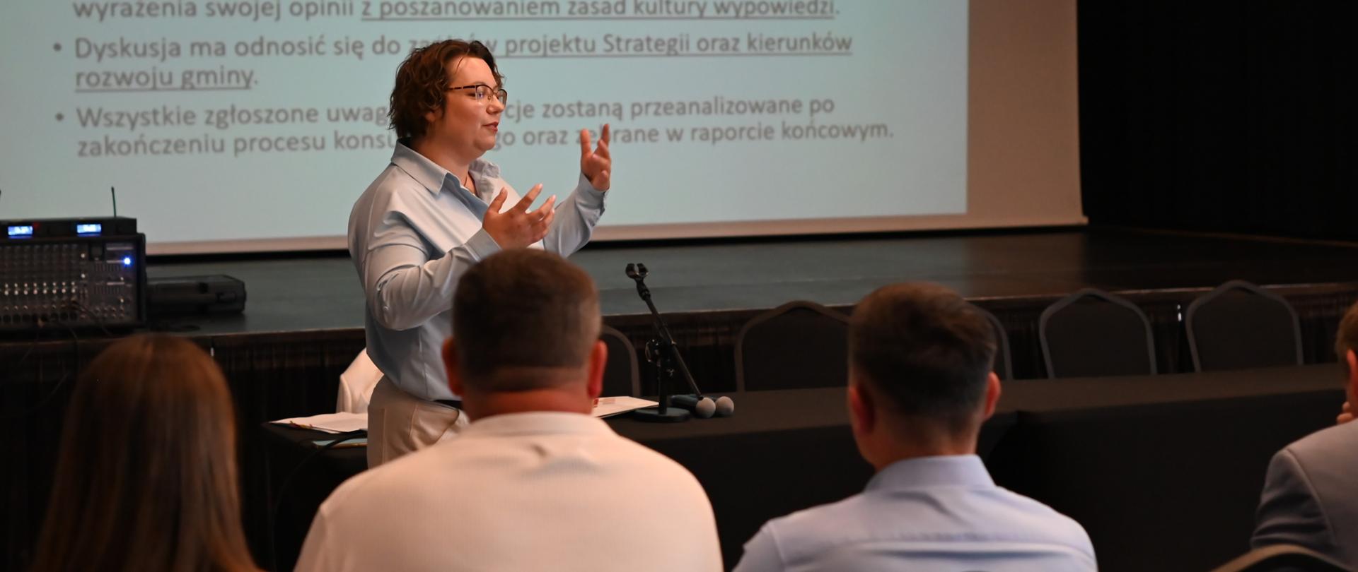 Kobieta prowadzi prezentację podczas spotkania konsultacyjnego dotyczącego strategii rozwoju gminy.