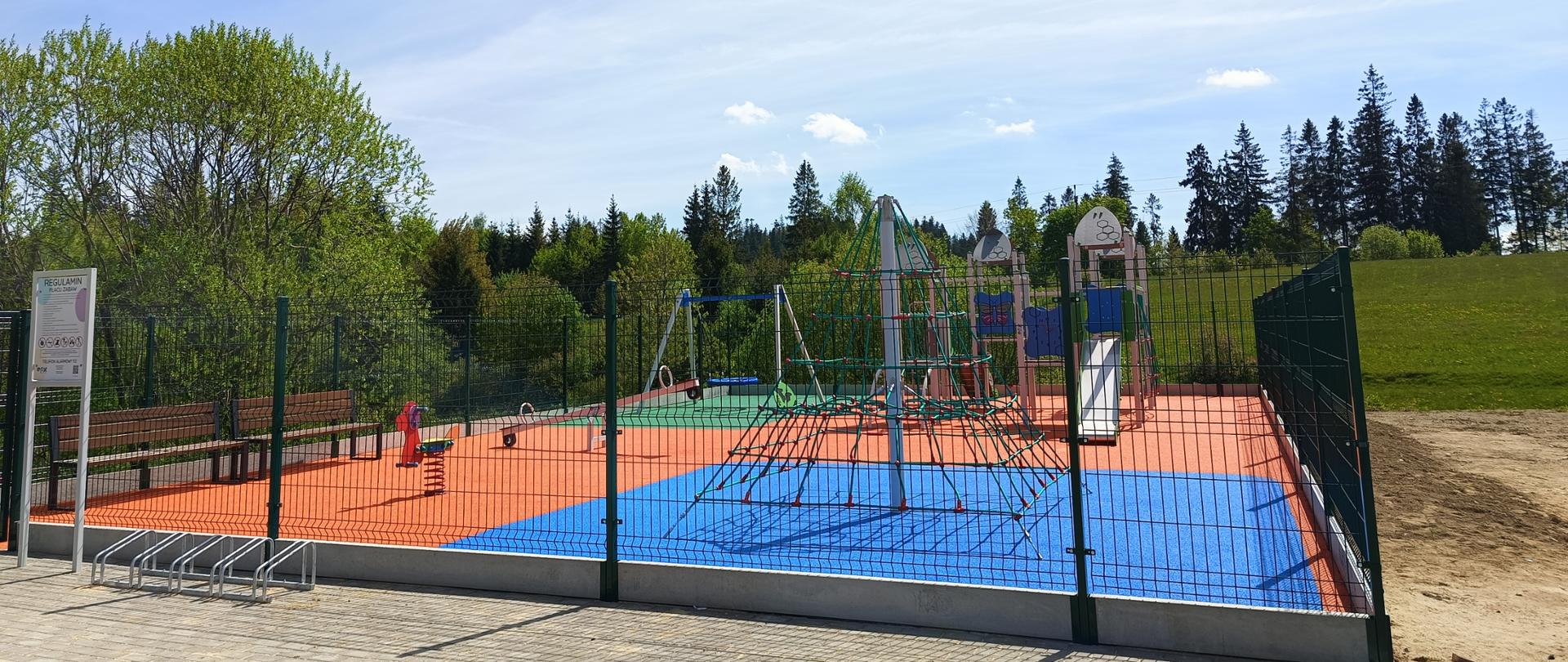 Zdjęcie przedstawia huśtawki, bujaki, piramidę oraz domek ze zjeżdżalnią na nowym placu zabaw w Bukowinie - Osiedla.