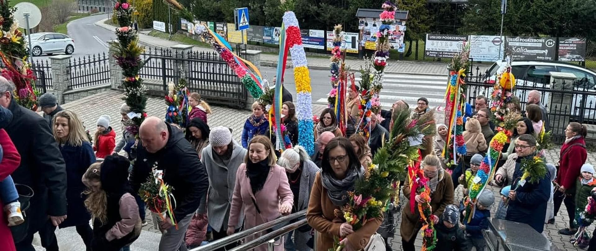 Zdjęcie przedstawia uczestników konkursu palmy wielkanocnej wchodzących do kościoła