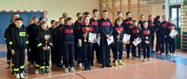 Grupa osób, drużyny młodzieżowe na sali gimnastycznej. Wszyscy ubrani w sportowe dresy. 