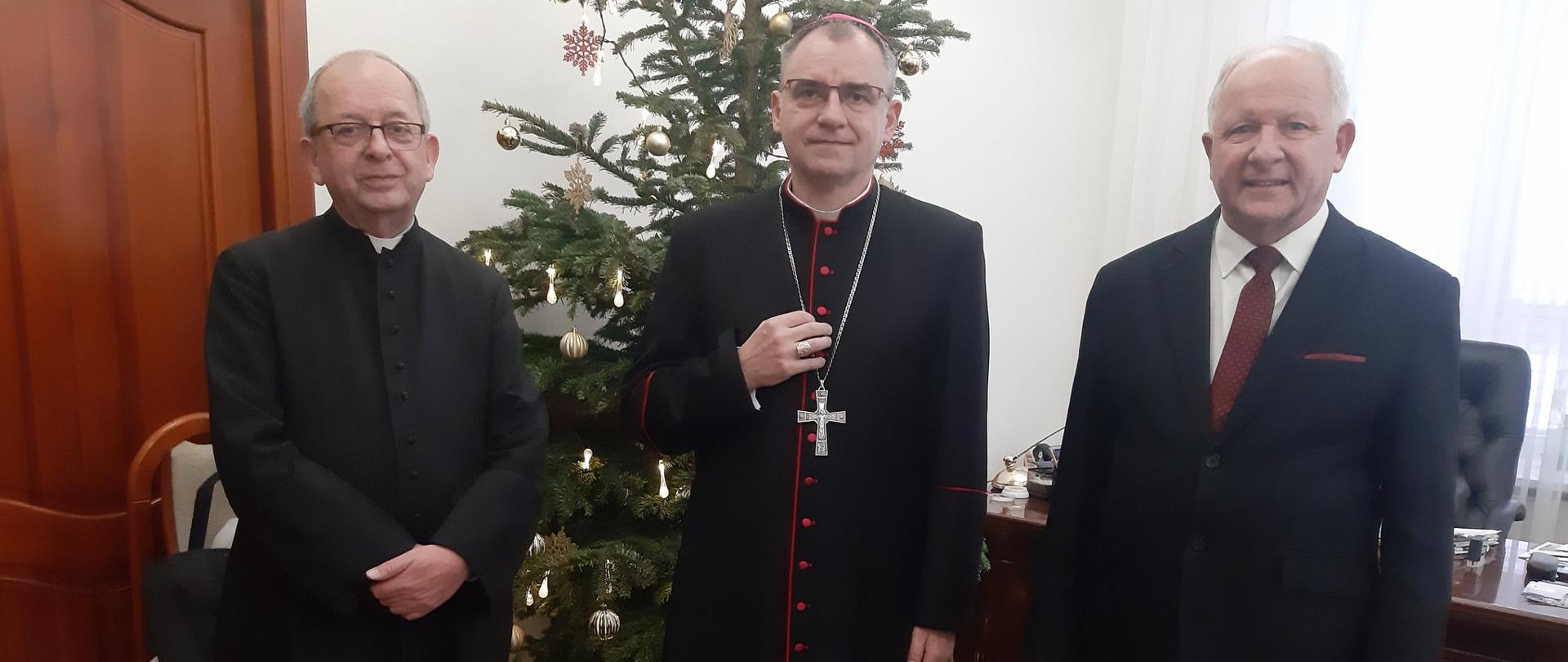 Na a fotografii na tle świątecznej choinki stoją od prawej: Burmistrz Miasta, Biskup Robert Chrząszcz, proboszcz