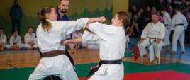 Dwie dziewczyny w tradycyjnych strojach kimono walczą w pozycji stojącej, wykonując ciosy rękoma.