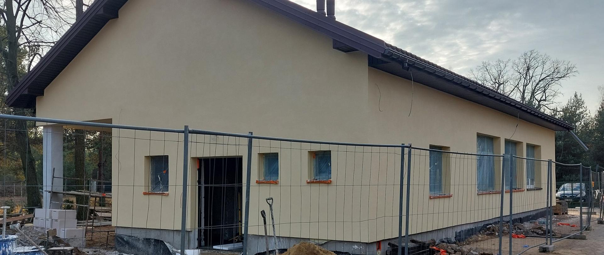 Żółty parterowy budynek. Wokół metalowe tymczasowe ogrodzenie.