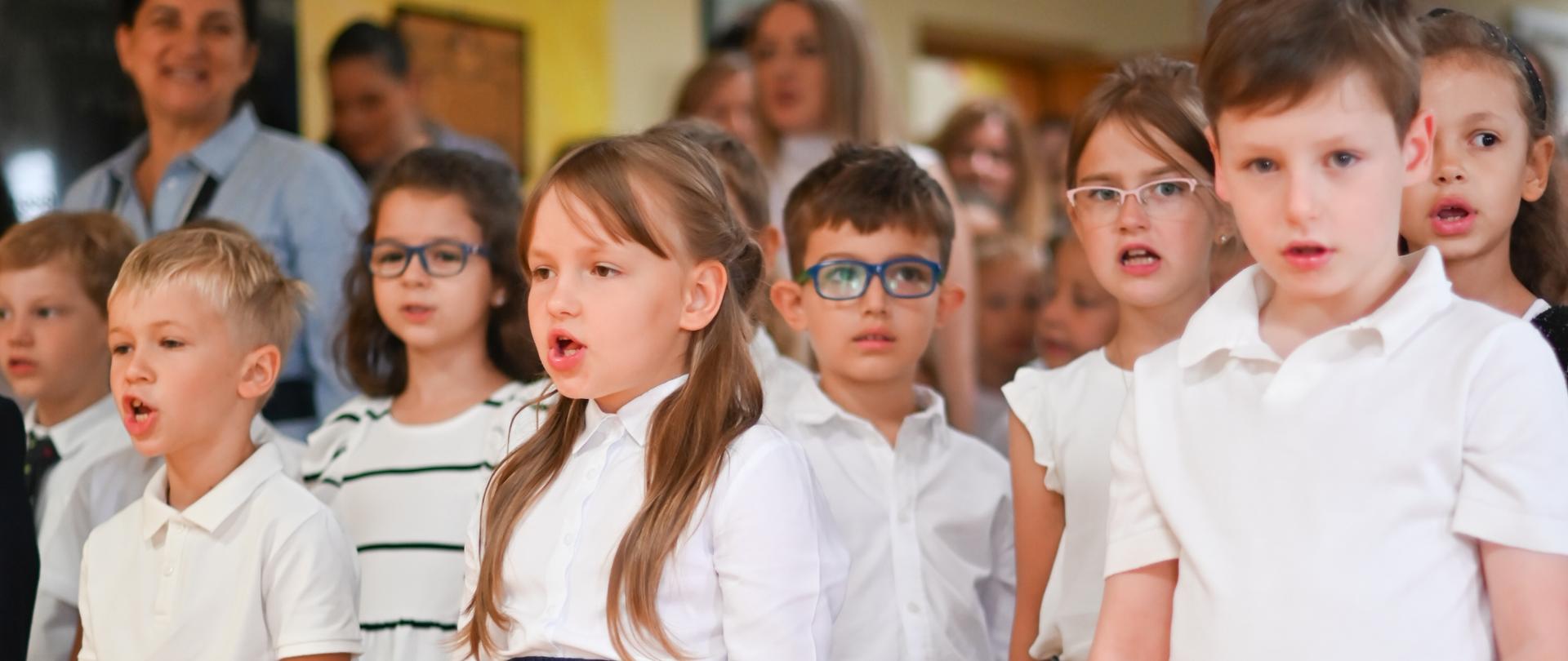 Grupa osób stoi w sali gimnastycznej podczas oficjalnej uroczystości.