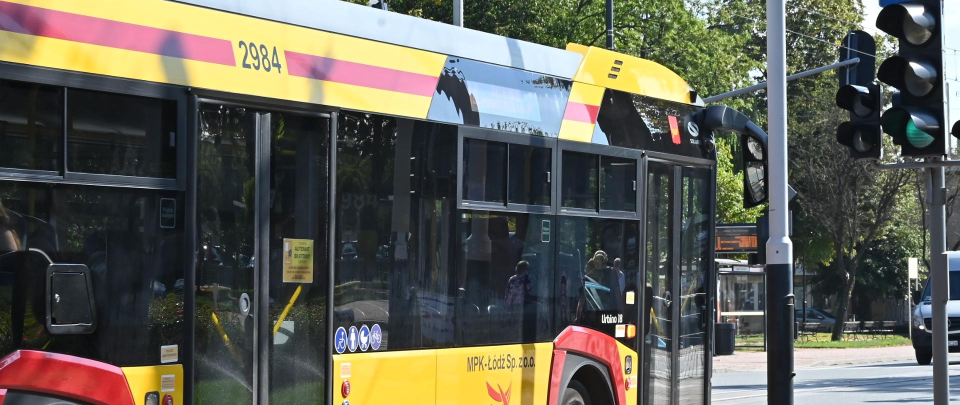 Autobus komunikacji miejskiej w barwach żółto-czerwonych z logo MPK Łódź stoi przy skrzyżowaniu na zielonym świetle.