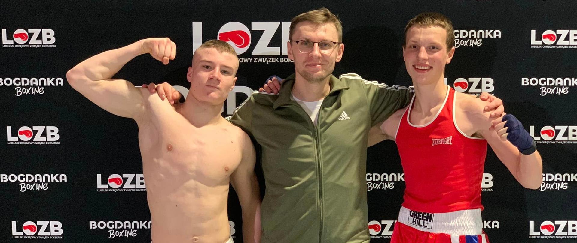 Na ściance Lubelskiego Okręgowego Związku Bokserskiego stoją od lewej: Patryk Zarębski, trener Michał Lenartowicz i Jan Wójcik