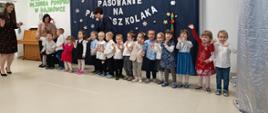 Przedszkolaki stoją w sali na tle ścianki "Pasowanie na przedszkolaka"