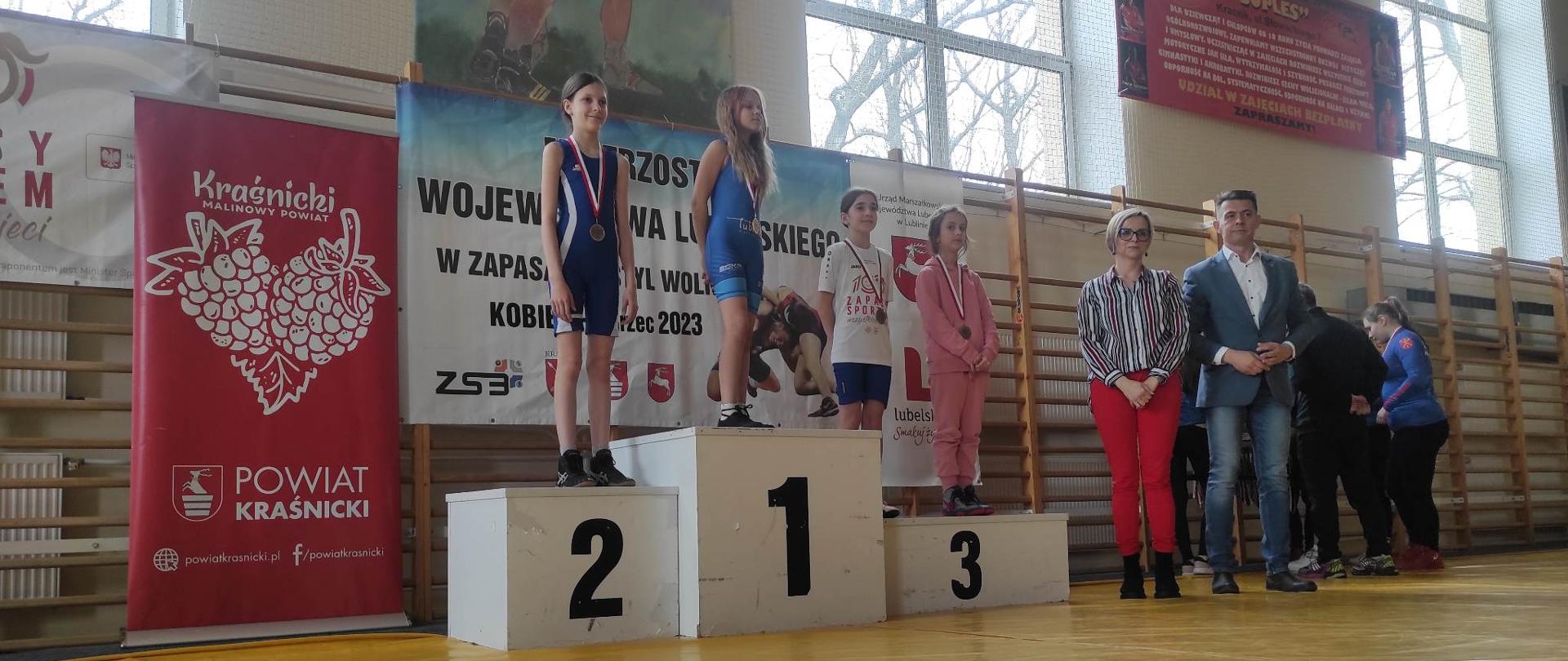 Uroczyste wręczanie medali. Na podium stoją zawodniczki w jednej z kategorii. Obok podium stoją: Dyrektor Zespołu Szkół nr 3 w Kraśniku Monika Gozdalska oraz Przewodniczący Rady Powiatu w Kraśniku Jacek Dubiel