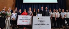 Osiemnaście osób pozujących do zdjęcia z tablicami informującymi o przyznaniu miejscowości Świetlino nagrody w wysokości 30 tysięcy złotych za zajęcie I miejsca w konkursie Piękna Wieś Pomorska 2025
