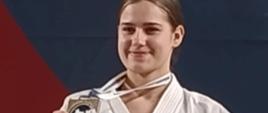 Martyna na Mistrzostwach Polski z medalem i dyplomem w ręku. Ubrana jest w tradycyjne kimono z czarnym pasem