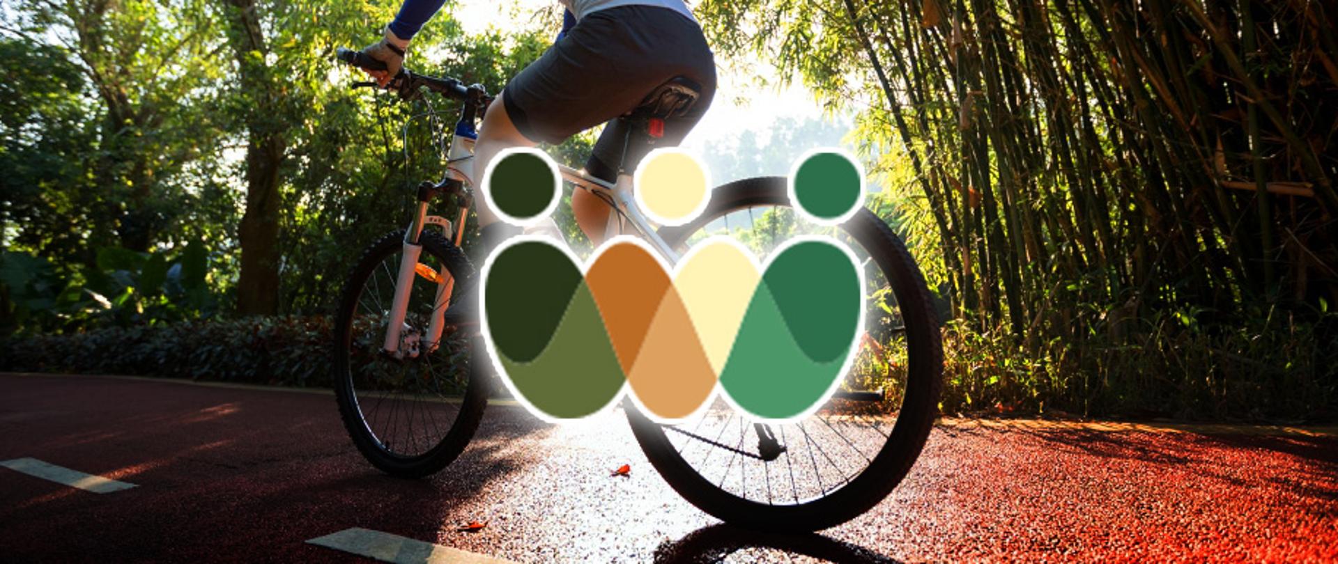 Zdjęcie rowerzysty jadącego ścieżką rowerową w słoneczny dzień, otoczony bujną zielenią. Na środku grafiki, na tle rowerzysty i roweru, umieszczone jest stylizowane logo Roztoczańskiego Związku Powiatowo-Gminnego w kształcie zachodzących na siebie kształtów w kolorach ziemi i zieleni przypominających trzy ludzkie sylwetki.