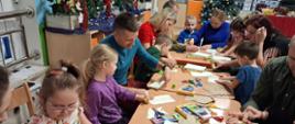Rodzice z dziećmi siedzą przy stole, przygotowują gwiazdy z papieru